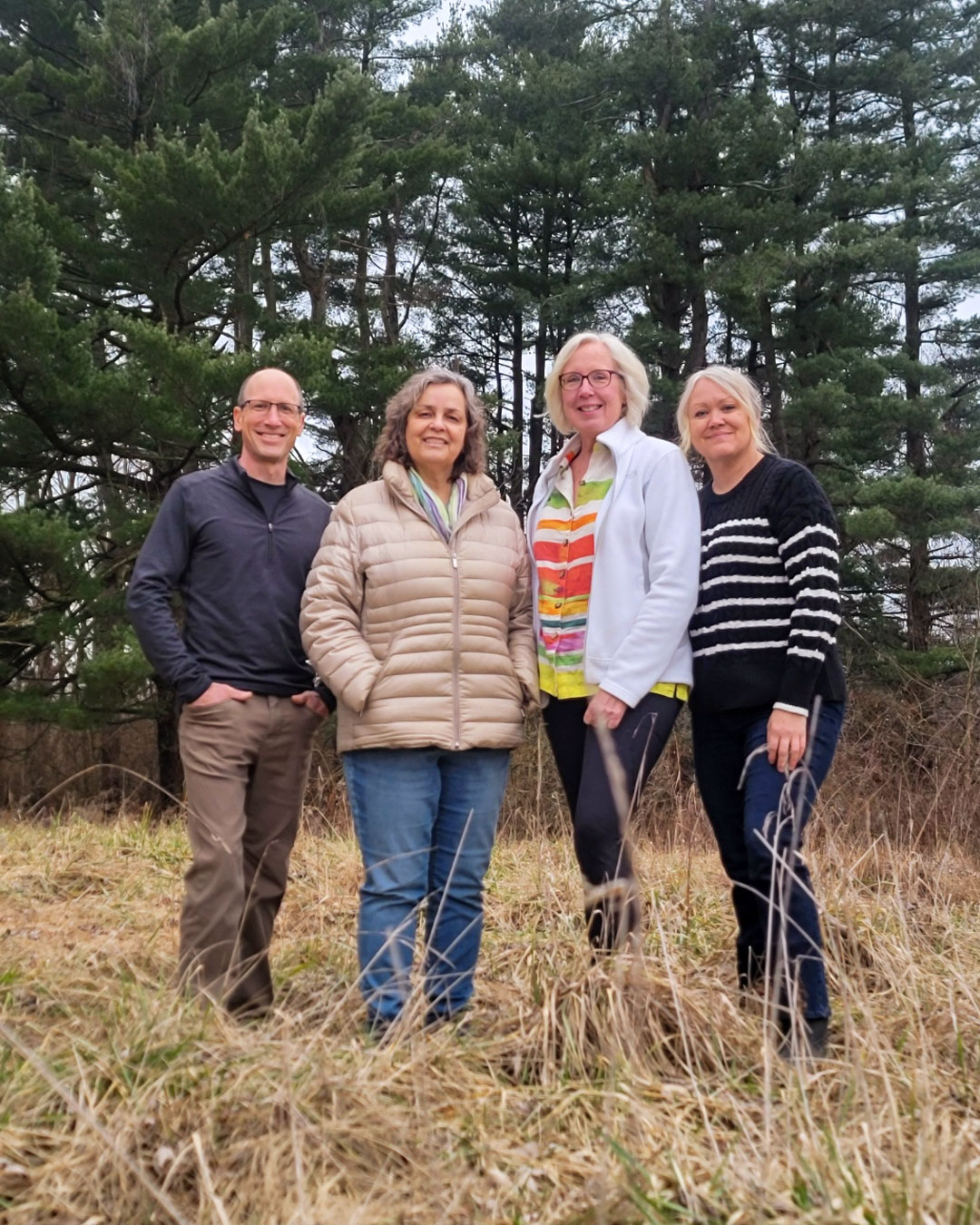 Article authors Lauren Enda, Kevin Kiley, Sharon Scovanner, and Jamie Smith standing in tall grass with pine trees in the background.